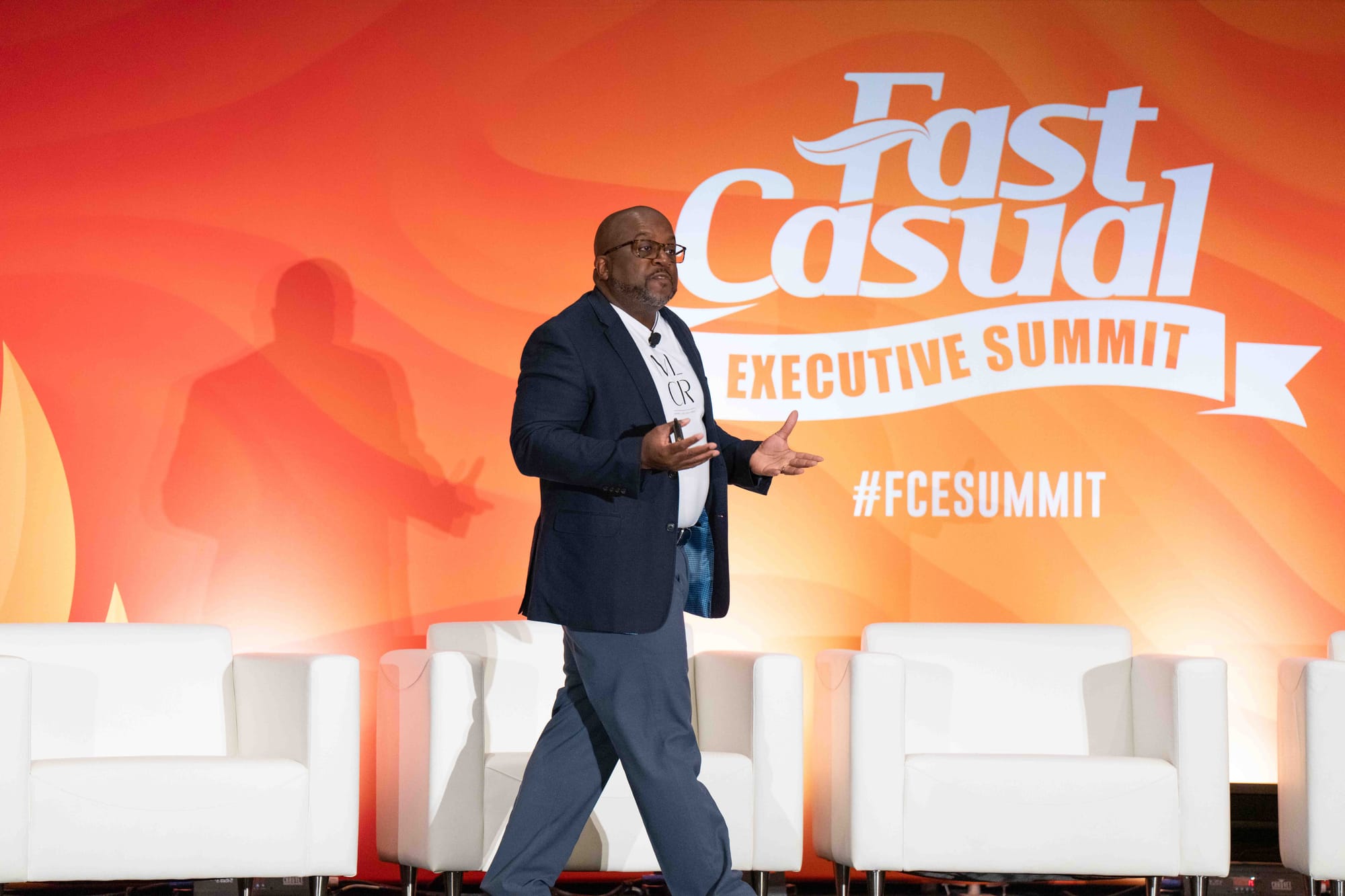 Jason E. Brooks speaking on the main stage at the Fast Casual Executive Summit, mid-gesture in front of a large event backdrop.