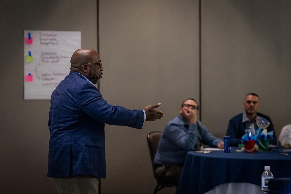 Jason E. Brooks leading a working session in a meeting room, gesturing toward two multi-unit leaders seated at a table.