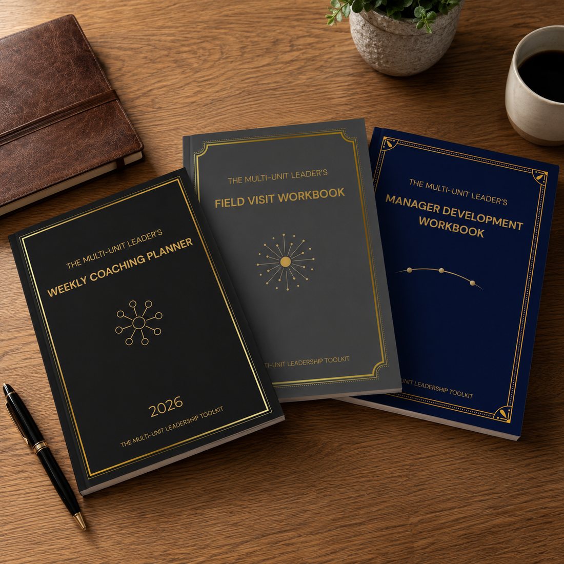 Three field-coaching workbooks on a wooden desk — the Weekly Coaching Planner, Field Visit Workbook, and Manager Development Workbook, in black, grey, and navy with gold detailing.